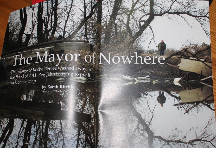 A man stands between trees looking out into a flooded plain that is full of rubble from recent moving floods. The image is by Tiffany Cassidy and is to illustrate a magazine story called the Mayor of Nowhere