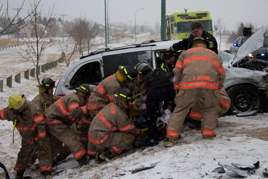 Six firefighters pull someone out of a damaged vehicle. Light snow is on the ground.